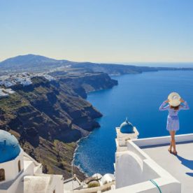 Young woman stands on a hill and looks at the marine landscape of Santorini, Greece