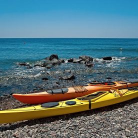 The yellow and orange kayaks on the black sand beach of Santorini, Greece