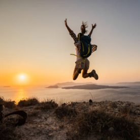 Rear view of a carefree female hiker having fun while jumping on a hill above the sea at sunset. Copy space.