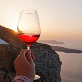 Hand holding a glass of a rose wine with a view to Santorini caldera.