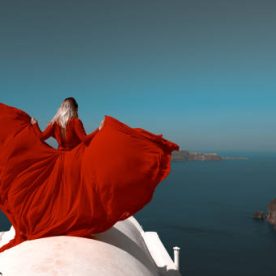 rear view of blond hair woman wearing red flying dress, posing in Santorini roof.