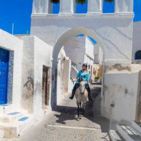 A girl rides a grey horse in a villa on the Greek island of Santorini